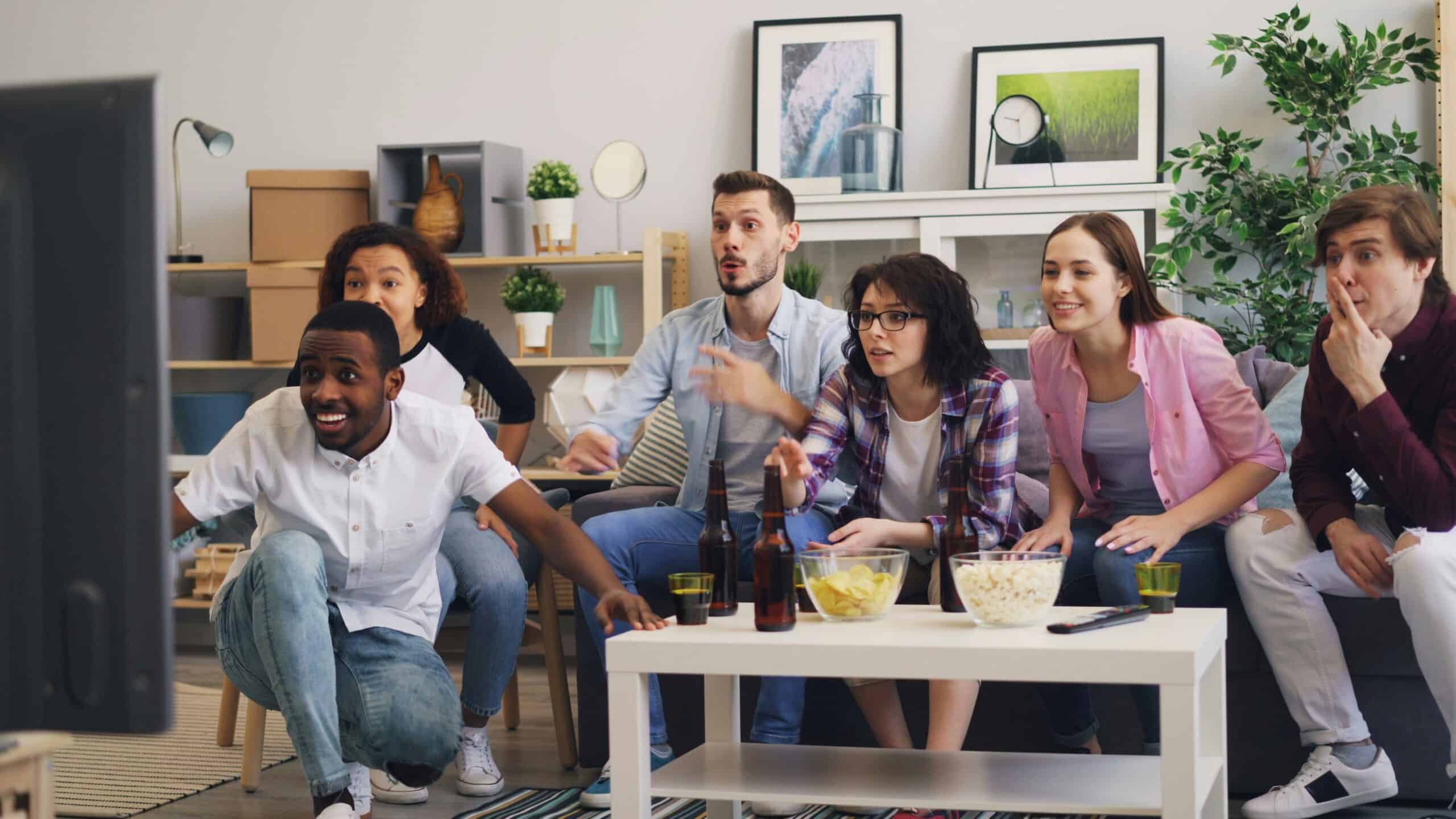 Group of diverse friends watching television and reacting excitedly at home.